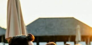 Resorts with Babysitting = Real Vacation for Parents a couple sipping cocktails by a pool at sunset while two kids play in the distance with a resort nanny